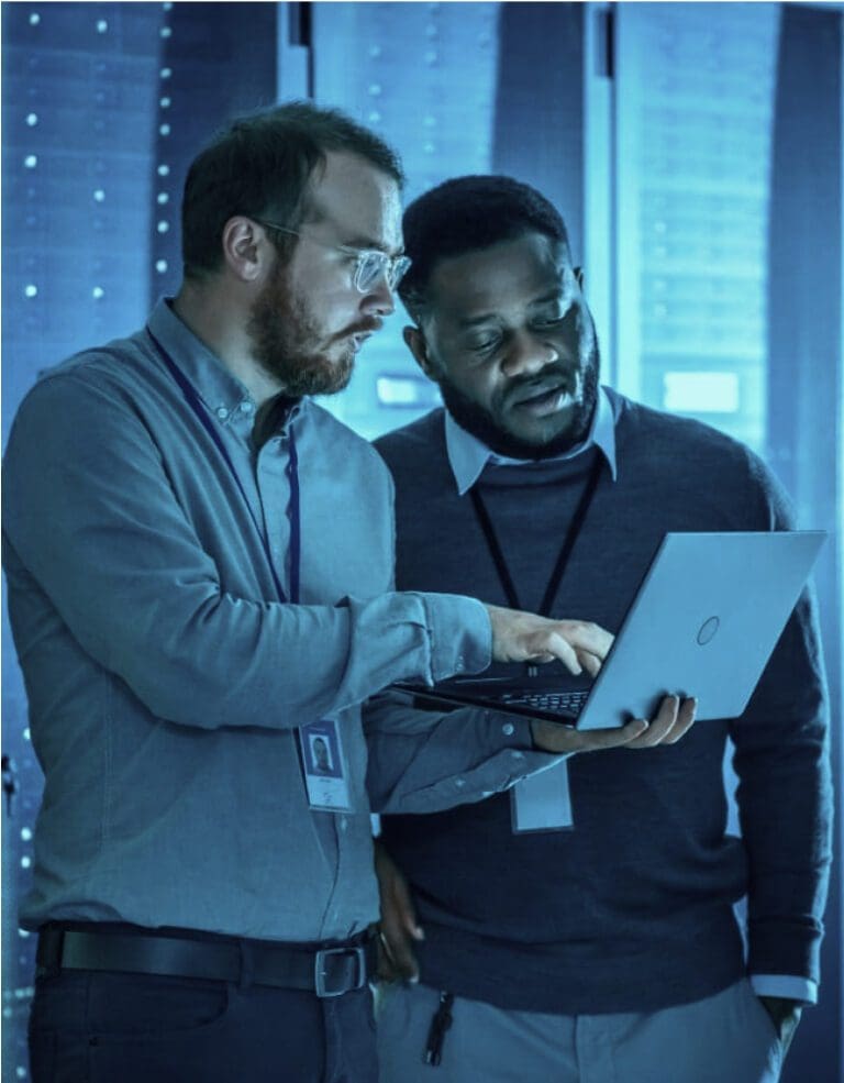Two men collaborating on laptop in data center.